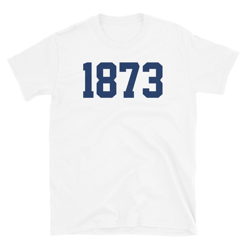 Puede incluir: Camiseta blanca con el n&uacute;mero 1873 impreso en azul marino.