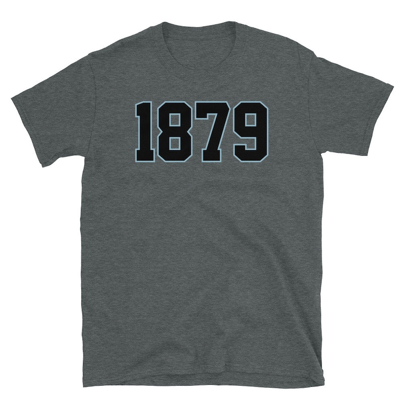 K&ouml;nnte beinhalten: Ein dunkelgraues T-Shirt mit dem Aufdruck 1879 in Schwarz mit hellblauem Umriss.