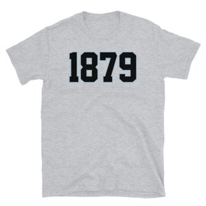 K&ouml;nnte beinhalten: Ein graues T-Shirt mit kurzen &Auml;rmeln und der Nummer 1879 in Schwarz auf der Vorderseite.