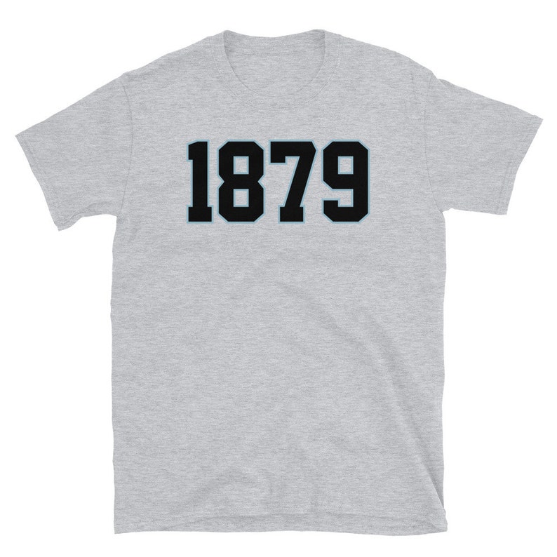 K&ouml;nnte beinhalten: Ein graues T-Shirt mit kurzen &Auml;rmeln und der Nummer 1879 in Schwarz auf der Vorderseite.