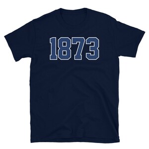 Puede incluir: Una camiseta azul marino con el n&uacute;mero 1873 impreso en blanco en la parte delantera.