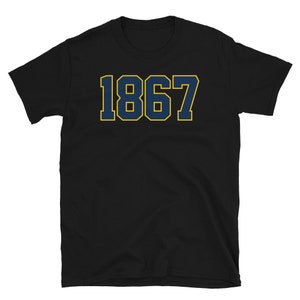 Może przedstawiać: Czarny T-shirt z nadrukiem 1867 w kolorze granatowym na przodzie, w pogrubionym, obwiedzionym kroju.