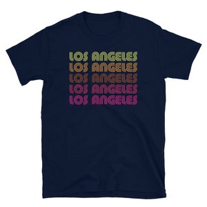 May include: A navy blue t-shirt with the text "Los Angeles" repeated five times in a retro, multi-colored font.