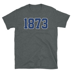Puede incluir: Una camiseta gris oscuro jaspeada con un 1873 azul marino impreso en la parte delantera.
