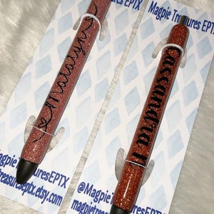 May include: Two rose gold glitter pens with black ink. The pens are personalized with the names "Malary" and "Cassanda".