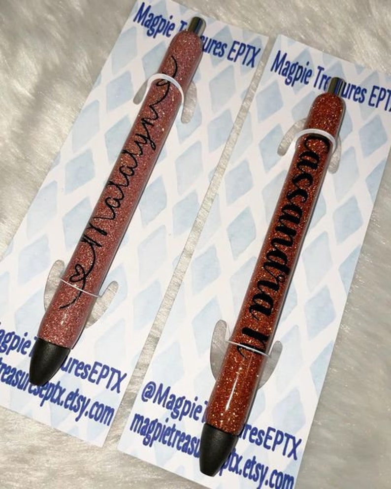 May include: Two rose gold glitter pens with black ink. The pens are personalized with the names "Malary" and "Cassanda".