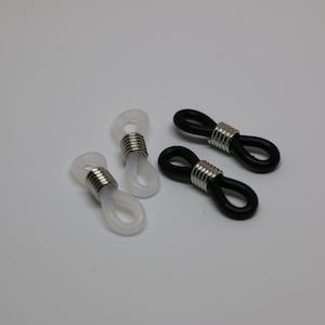 May include: Four eyeglass retainers. Two are white, and two are black. Each retainer has a silver metal coil around the loop. The retainers are designed to hold the arms of eyeglasses.