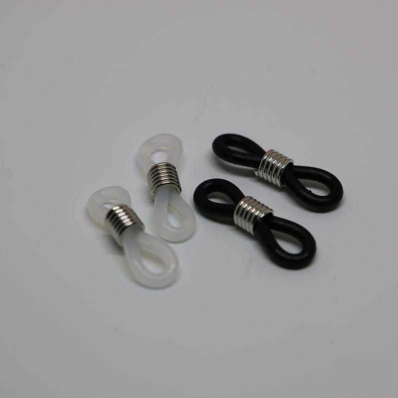 May include: Four eyeglass retainers. Two are white, and two are black. Each retainer has a silver metal coil around the loop. The retainers are designed to hold the arms of eyeglasses.