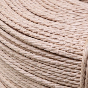 Pode incluir: Close-up de um rolo de corda bege natural enrolado firmemente. A corda é feita de um material tecido e tem uma textura ligeiramente áspera.
