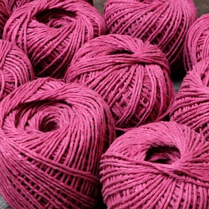 May include: A close-up of several balls of pink yarn, each wound into a tight coil. The yarn is a deep, rich pink color and has a slightly textured surface.