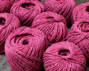 May include: A close-up of several balls of pink yarn, each wound into a tight coil. The yarn is a deep, rich pink color and has a slightly textured surface.