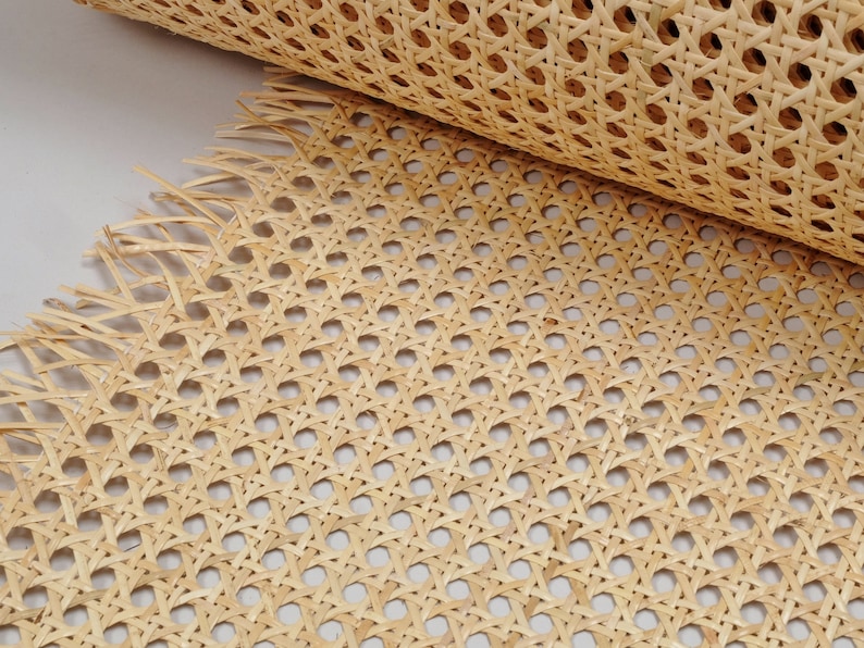 May include: A roll of light tan natural cane webbing featuring a classic octagonal woven pattern. The material displays a consistent grid of small holes formed by interlaced strips of plant fiber, with frayed edges visible at the bottom.