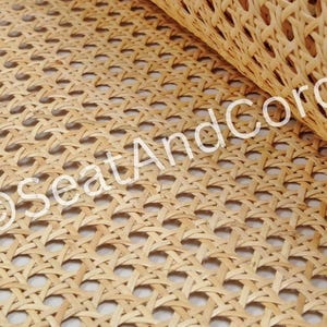May include: A roll of light tan natural cane webbing featuring a consistent octagonal woven pattern. The material is flexible and displays a repeating open grid structure. The text SeatAndCord is printed in white across the surface of the material.