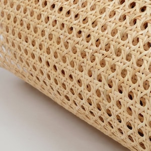 May include: A roll of light beige cane webbing featuring a consistent octagonal woven pattern. The material is made of thin, flexible strips of natural plant fiber, creating a semi-transparent, open-grid texture across the entire surface.
