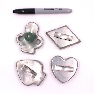 May include: Four metal cookie cutters shaped like playing card suits: a heart, a diamond, a spade, and a club. The club cutter has a green plastic handle.