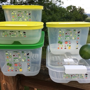 May include: Four clear plastic containers with yellow lids and green accents. The containers have a sticker with a variety of fruits and vegetables on them. A lime is sitting on top of one of the containers.