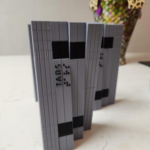 May include: A stack of gray plastic cards with black rectangular shapes and braille dots. The top card has the word "TARS" printed on it.