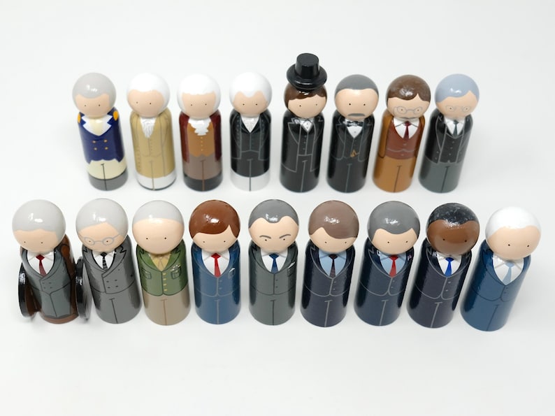 May include: A set of wooden peg dolls, each depicting a person in formal wear. The dolls display diverse skin tones, hairstyles, and suit colours, such as black, grey, blue, and brown. Some dolls have ties, and one is wearing a top hat.
