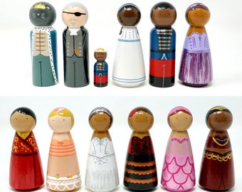 May include: A collection of hand-painted wooden peg dolls. The dolls feature various designs, including a cat king, a pirate, and figures in dresses and uniforms. The color palette includes blue, red, white, and gold. These dolls are suitable for display or play.