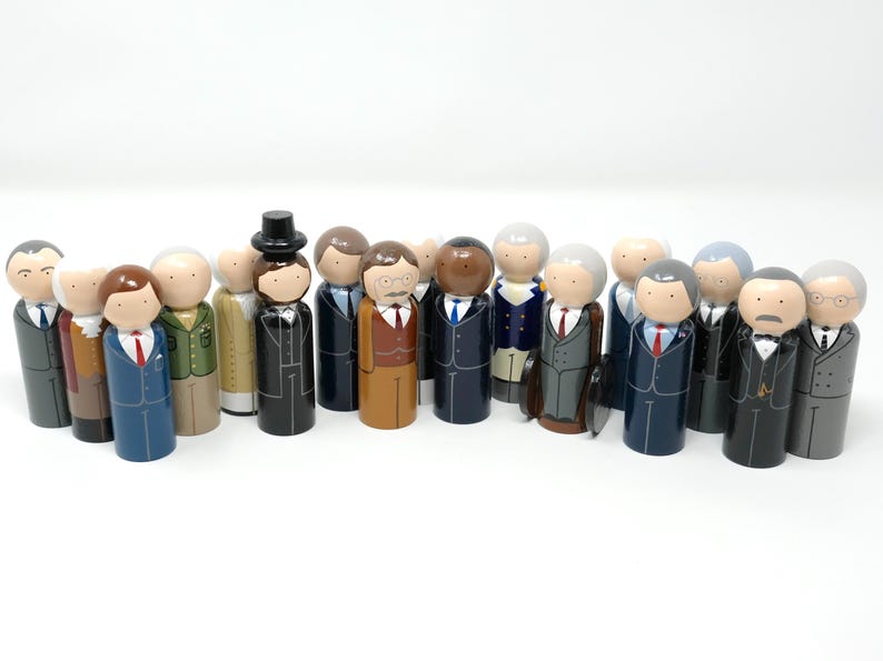 May include: A group of painted wooden peg dolls, each wearing a suit and tie. The dolls have different skin tones and suit styles, some with hats or briefcases. The figures are arranged together, possibly representing a meeting or a collection.