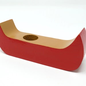 May include: A wooden canoe-shaped candle holder. The exterior is painted red, while the interior and the area around the candle hole are natural wood. The candle holder is designed to hold a single candle.