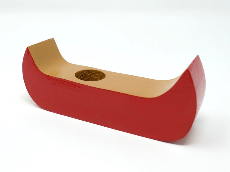 May include: A wooden canoe-shaped candle holder. The exterior is painted red, while the interior and the area around the candle hole are natural wood. The candle holder is designed to hold a single candle.