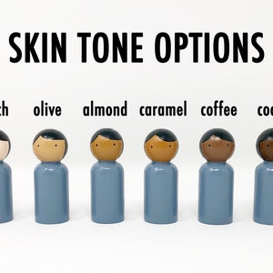 May include: Six wooden peg dolls with varying skin tones are displayed: peach, olive, almond, caramel, coffee, and cocoa. Each doll has a blue body and black hair. The text "SKIN TONE OPTIONS" is above the dolls.