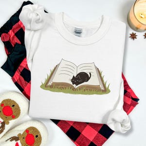 本好きのTシャツ、クルーネックスウェットシャツ、本の上に横たわるかわいい猫と花の刺繍スウェットシャツ、花と猫の刺繍パーカー。