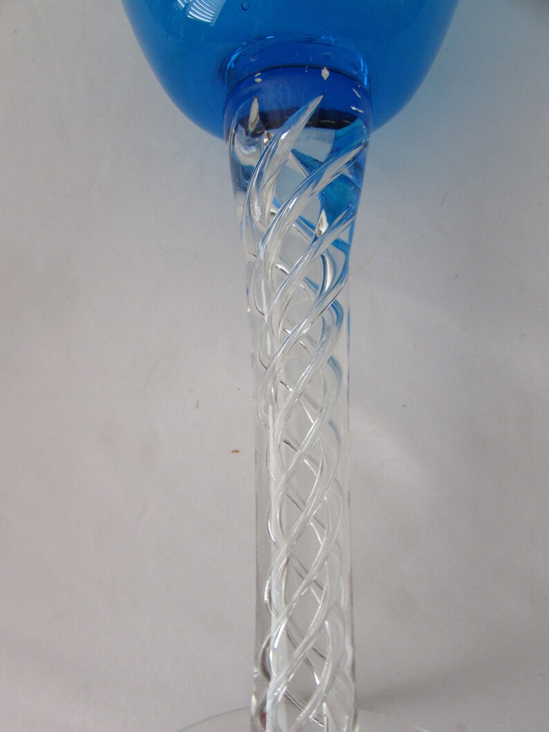 K&ouml;nnte beinhalten: Ein Glaspokal mit einer leuchtend blauen Kuppa und einem klaren Stiel, der ein komplexes, in sich gedrehtes Glasgitterdesign aufweist. Der Stiel ist mit der Basis der blauen Kuppa verbunden und zeigt ein detailliertes Spiralmuster im Glas.