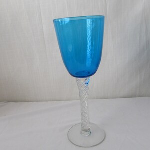 K&ouml;nnte beinhalten: Ein hohes Trinkglas mit einer leuchtend blauen Kuppa und einem klaren Glasstiel, der ein komplexes, in sich gedrehtes Gittermuster aufweist. Der Stiel ist mit einem runden, flachen Fu&szlig; aus klarem Glas verbunden, was eine ausgewogene Form ergibt.