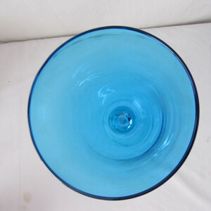 K&ouml;nnte beinhalten: Eine Draufsicht auf einen Kelch oder eine Vase aus leuchtendem, durchscheinendem t&uuml;rkisblauem Glas. Die kreisf&ouml;rmige &Ouml;ffnung gibt den Blick auf eine glatte, klare Innenfl&auml;che frei, die sich zur Basis hin verj&uuml;ngt und die Farbe des Glases zeigt.