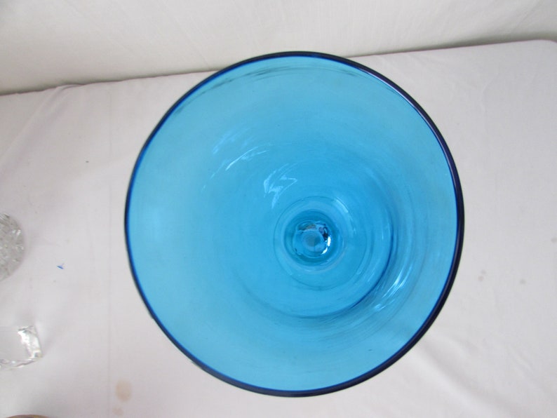 K&ouml;nnte beinhalten: Eine Draufsicht auf einen Kelch oder eine Vase aus leuchtendem, durchscheinendem t&uuml;rkisblauem Glas. Die kreisf&ouml;rmige &Ouml;ffnung gibt den Blick auf eine glatte, klare Innenfl&auml;che frei, die sich zur Basis hin verj&uuml;ngt und die Farbe des Glases zeigt.