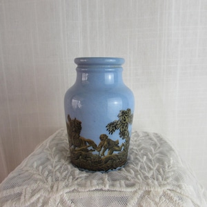 Puede incluir: Un jarrón de cerámica azul claro con una escena de monos en un bosque pintada en la parte delantera.