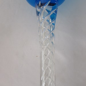 K&ouml;nnte beinhalten: Ein Glaspokal mit einer leuchtend blauen Kuppa und einem klaren Stiel, der ein komplexes, in sich gedrehtes Glasgitterdesign aufweist. Der Stiel ist mit der Basis der blauen Kuppa verbunden und zeigt ein detailliertes Spiralmuster im Glas.