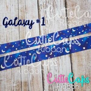 May include: Two rolls of blue and white galaxy-themed ribbon with silver glitter moons and stars. The ribbon is labeled "Galaxy #1" and "Cutie Caps Ribbon".