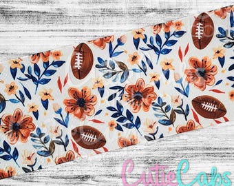 May include: White ribbon with a floral pattern featuring orange flowers, blue leaves, and brown footballs.