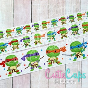 May include: White ribbon with a repeating pattern of Teenage Mutant Ninja Turtles characters. The turtles are wearing their signature bandanas and holding weapons. The ribbon is decorated with colorful confetti.