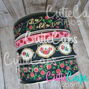 May include: A stack of four black and white ribbon rolls with rose patterns. The top ribbon has gold lettering that reads "Talk as old as time".