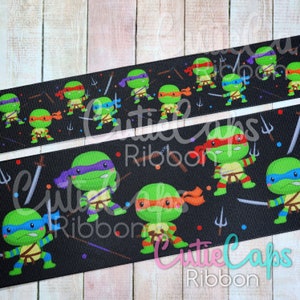 May include: Black and white ribbon with a repeating pattern of Teenage Mutant Ninja Turtles characters. The turtles are wearing their signature bandanas and holding weapons. The ribbon is decorated with stars and other small details.