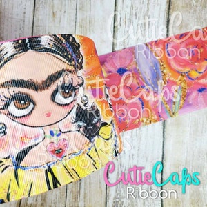 May include: A colorful ribbon featuring a cartoon illustration of Frida Kahlo with a black cat. The ribbon has a pink background with gold glitter accents. The text "Cutie Caps Ribbon" is visible in the bottom right corner of the image.