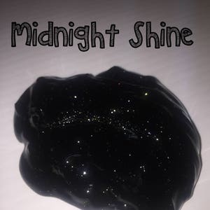 May include: Black slime with glitter, labeled "Midnight Shine". The dark, glossy slime has a textured surface and is speckled with shimmering particles. The image is set against a white background.