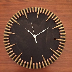 May include: A black circular clock with a wooden face and bullet casings around the edge. The clock hands are white.