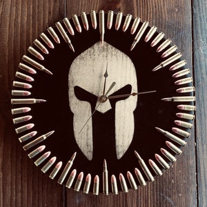 May include: A black clock with a Spartan helmet design. The clock face is surrounded by a ring of bullet casings.