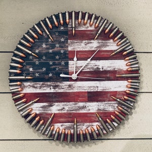 May include: A round clock with an American flag design. The clock face is made of wood and has a distressed look. The numbers are made of bullet casings.