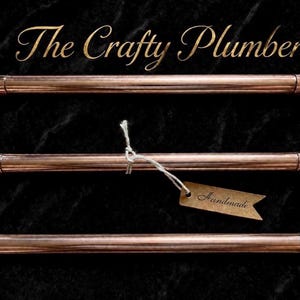 Puede incluir: Un marco rectangular construido con tuberías y accesorios de cobre pulido. El texto The Crafty Plumber se muestra sobre el marco. Una pequeña etiqueta de papel marrón con la palabra Handmade está unida a la barra central con un hilo blanco.