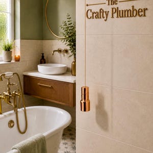 May include: A bathroom interior with a white bathtub, a wooden vanity unit with a white basin, and a circular gold mirror. The wall features the gold text "The Crafty Plumber", and a copper-toned pull cord hangs down.