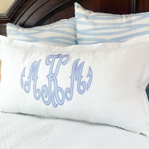 Peut inclure: Oreiller rectangulaire blanc avec un monogramme bleu clair. Le monogramme présente les lettres M, K et M dans une écriture décorative. Deux oreillers avec un motif de vagues bleues et blanches sont en arrière-plan.