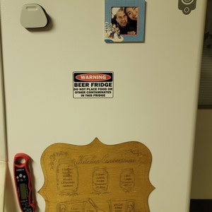 May include: A white refrigerator with a wooden sign that says "Kitchen Conversions" and has various measurements for cups, pints, quarts, and ounces. There is a warning sign that says "Beer Fridge Do Not Place Food or Other Contaminates in This Fridge".