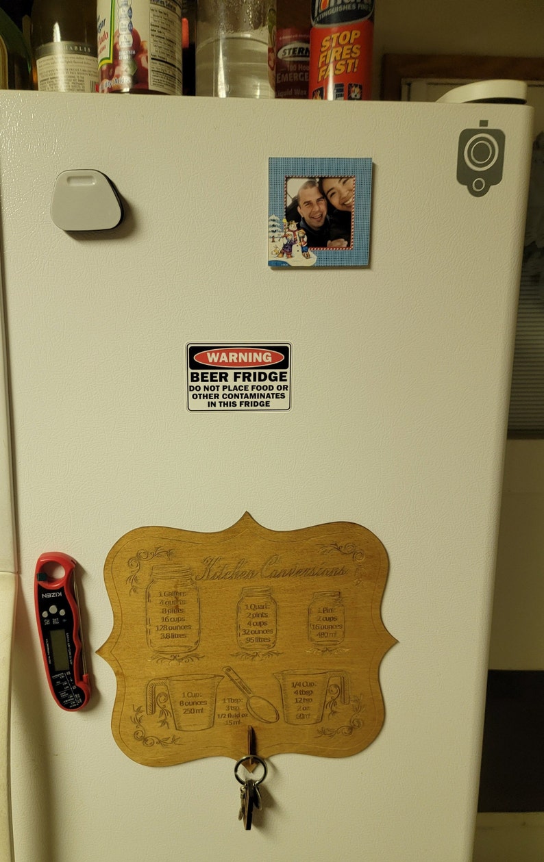May include: A white refrigerator with a wooden sign that says "Kitchen Conversions" and has various measurements for cups, pints, quarts, and ounces. There is a warning sign that says "Beer Fridge Do Not Place Food or Other Contaminates in This Fridge".