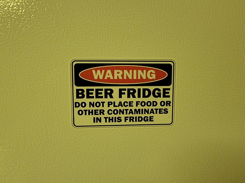 May include: A black and red warning sign on a yellow surface that reads "WARNING BEER FRIDGE DO NOT PLACE FOOD OR OTHER CONTAMINATES IN THIS FRIDGE".
